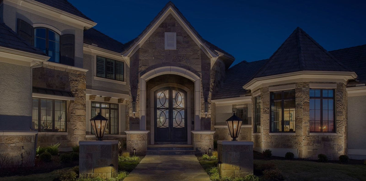Exterior lantern and landscape lighting on a stone house at dusk